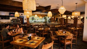 Ein Restaurantinneres mit Holztischen und -stühlen, hängenden Korbtischen und einem Barbereich mit einem sichtbaren ESPN-Bildschirm.