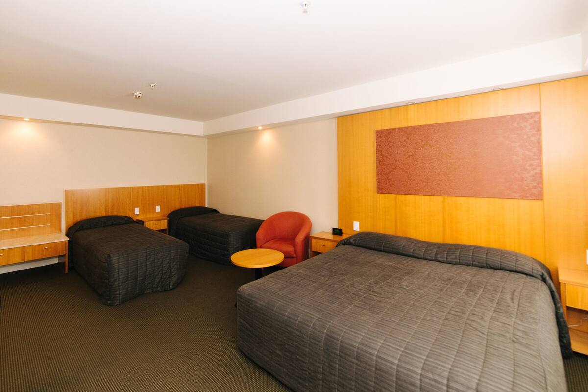 Una habitación de hotel con dos camas, una mesita, una silla y un cabecero de madera.
