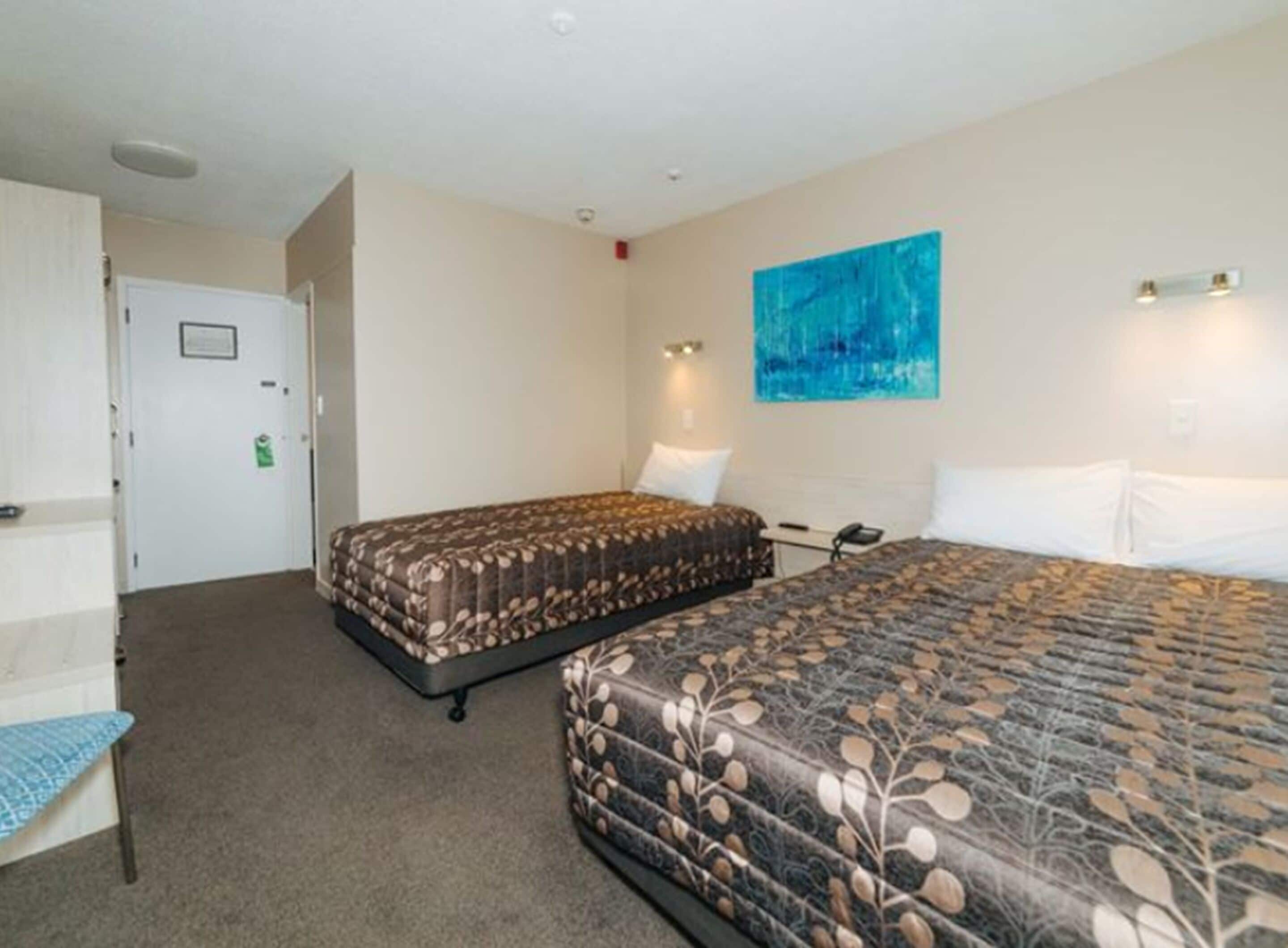 A hotel room with two beds, a desk, a chair, and a painting on the wall.