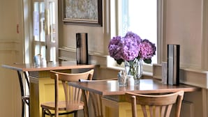 Un coin repas avec des tables et des chaises en bois, un vase rempli de fleurs violettes et une œuvre d’art encadrée accrochée au mur.