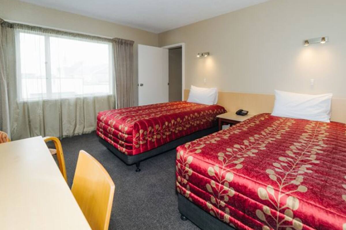 Quarto de hotel com duas camas, uma escrivaninha e uma cadeira.
