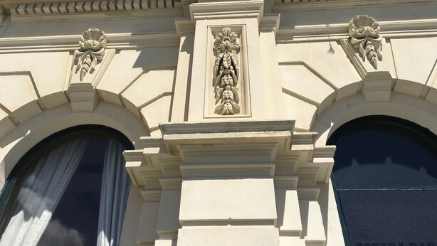 Une façade d’immeuble ornée de détails architecturaux raffinés, comprenant un panneau décoratif central et deux sculptures symétriques.