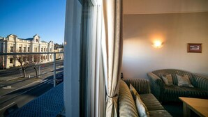 Un balcon donnant sur une rue de la ville et sur des immeubles, un canapé et un luminaire fixé au mur.