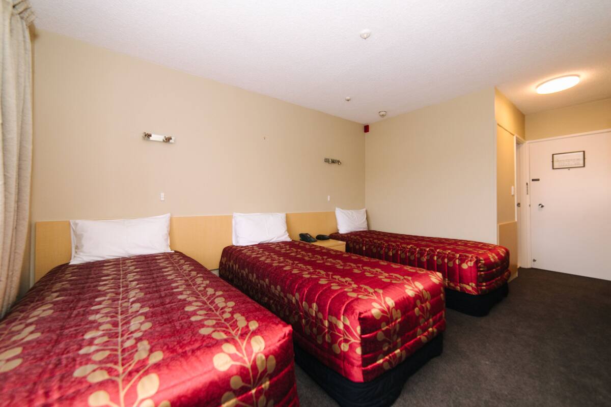 Quarto de hotel com três camas, paredes bege e uma porta.