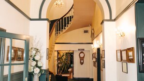 Un couloir avec un escalier, une horloge et des tableaux encadrés accrochés aux murs.