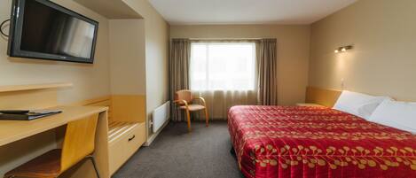 A hotel room with a bed, a desk, a chair, a television, and a window with curtains.