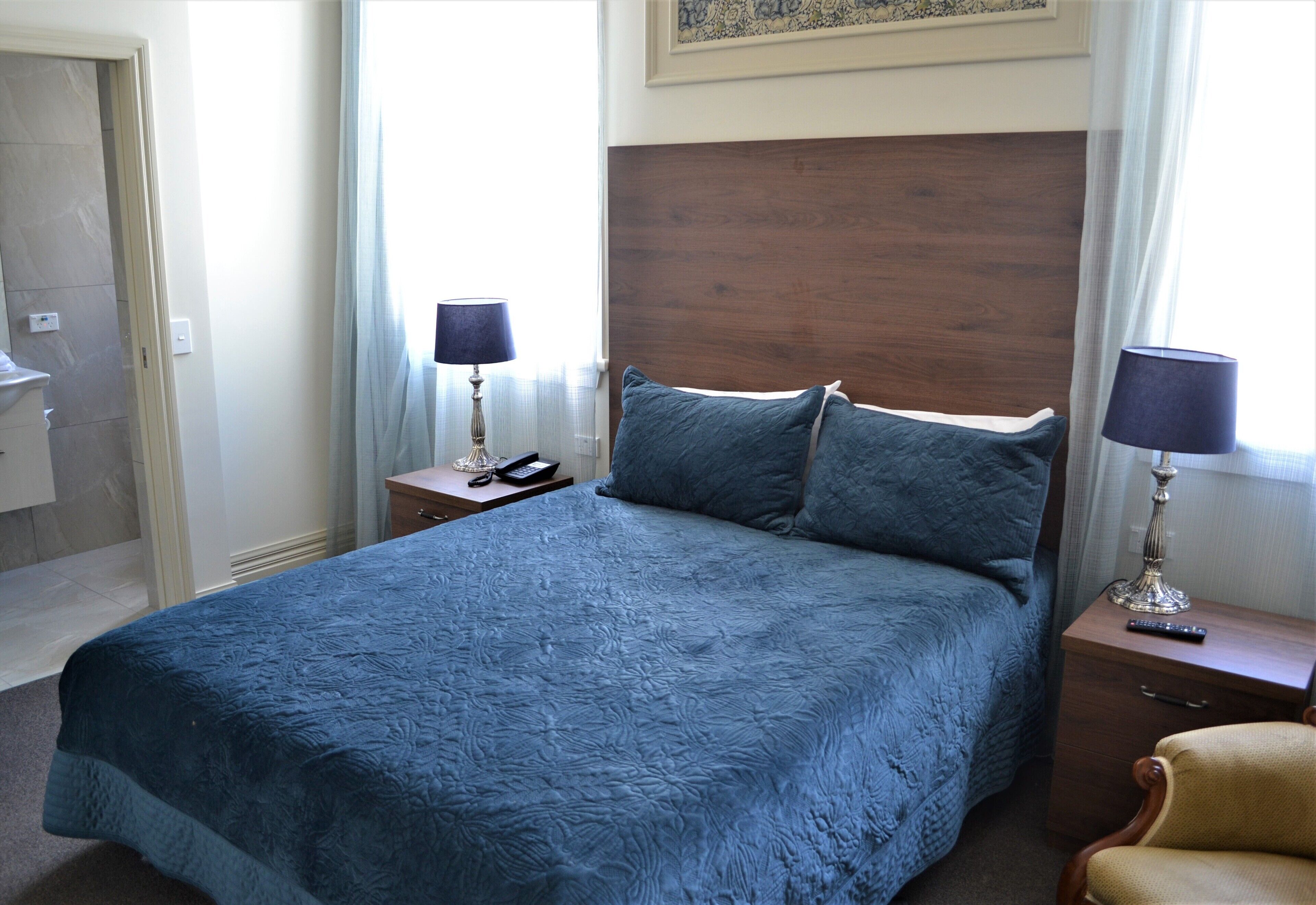 A bedroom with a large bed, two bedside tables, a nightstand, a chair, and a window with curtains.