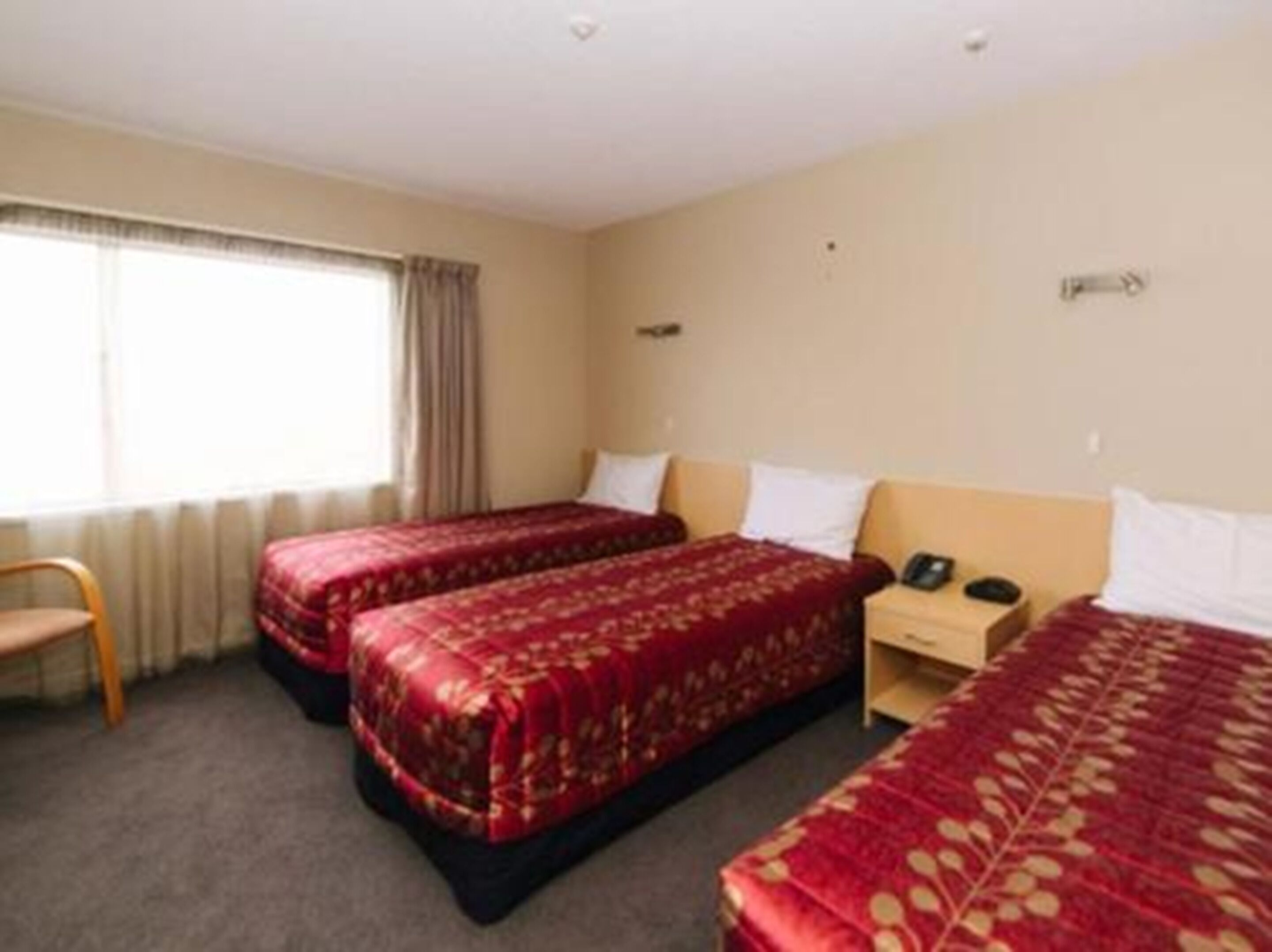 Een hotelkamer met twee enkele bedden, een houten nachtkastje, een stoel en een raam met gordijnen.