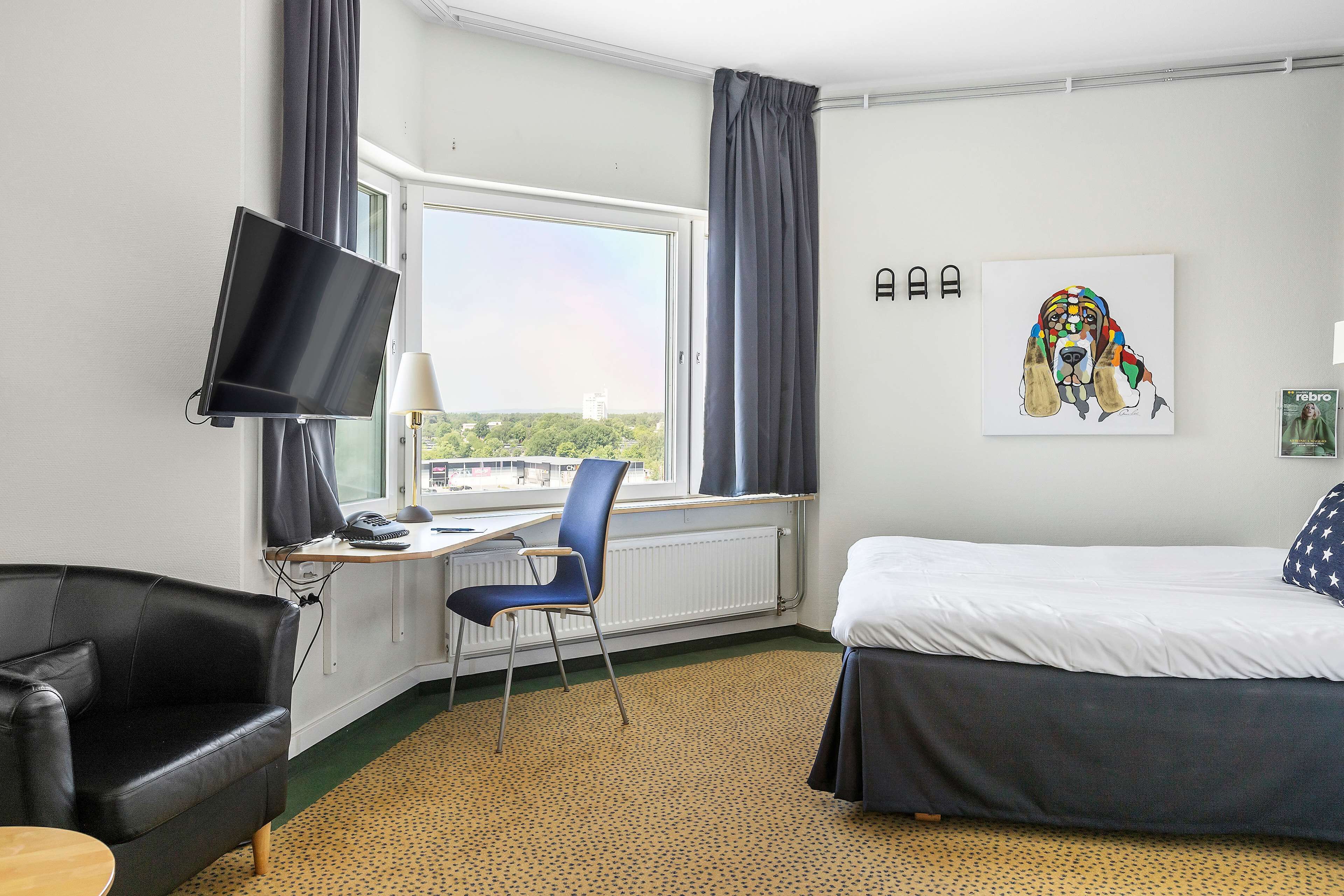 A hotel room with a bed, a desk with a chair, a TV, and a window with curtains.