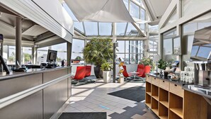 A modern reception area with a glass ceiling, red chairs, a large plant, and a counter with various amenities. - Best Western Eurostop Orebro (Örebro)
