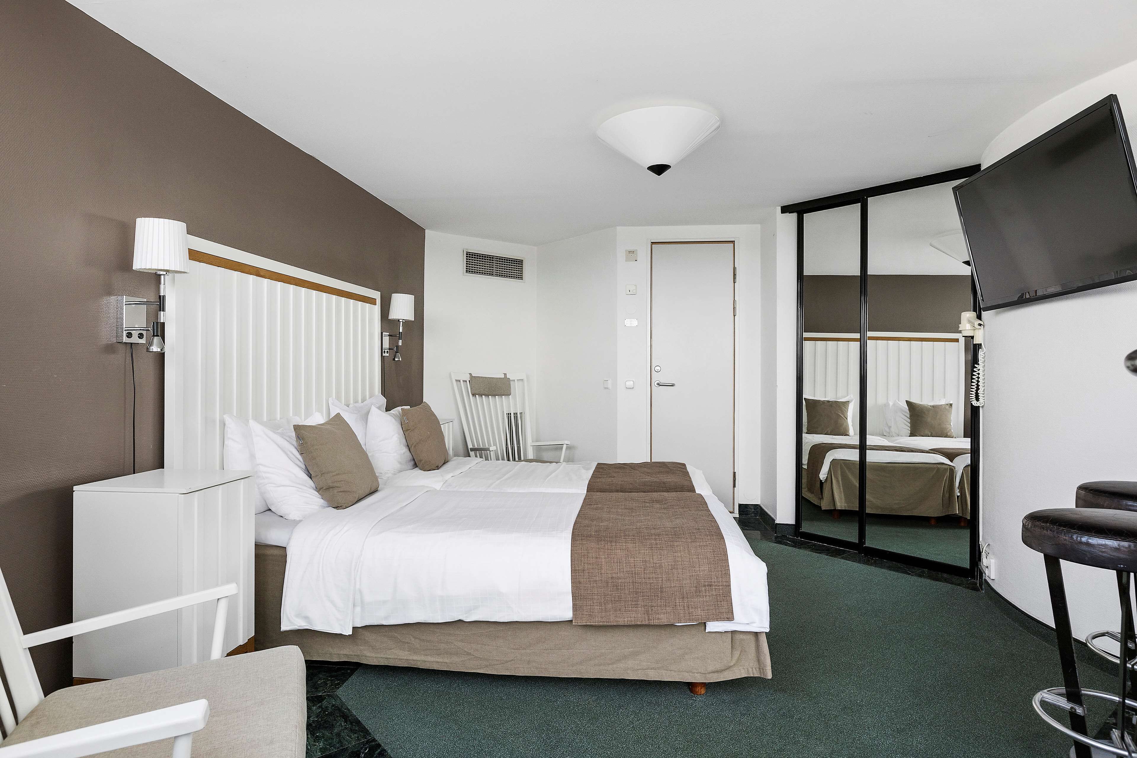 A hotel room with a bed, bedside tables, a TV, and a mirror.