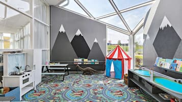 Explore a vibrant learning space with colorful carpet, play tables, and a bookshelf filled with children's books.