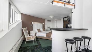 Une chambre d’hôtel moderne équipée d’un lit, d’une chaise, d’un bureau et d’un coin bar avec des tabourets.