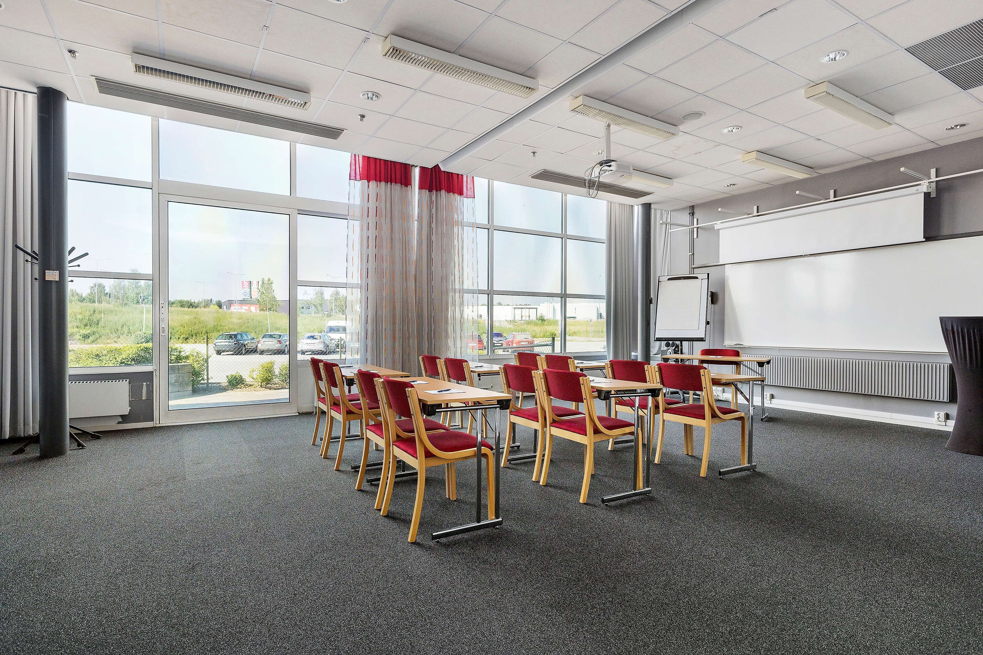 Un salón de conferencias con ventanas amplias, una pizarra y sillas rojas.