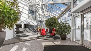 A modern indoor space with a glass ceiling, red chairs, and potted plants. - Best Western Eurostop Orebro (Örebro)