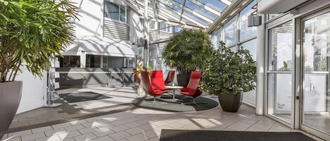 A modern indoor space with a glass ceiling, red chairs, and potted plants.