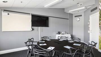 Ett konferensrum med ett runt bord, åtta stolar, en whiteboard, en platt-TV och en väggklocka.