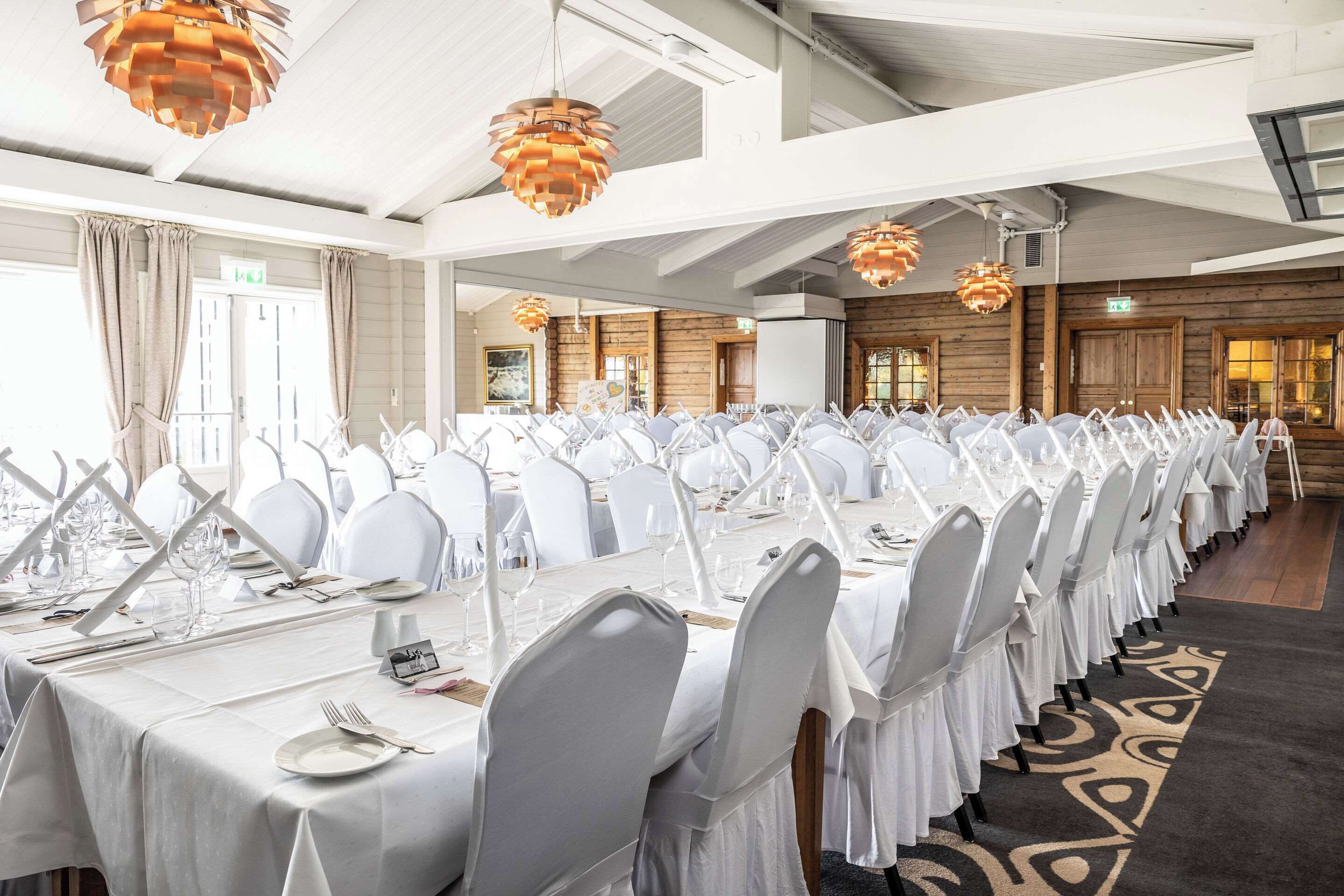 A long banquet table set for a formal event, with white tablecloths, chairs, and glassware.