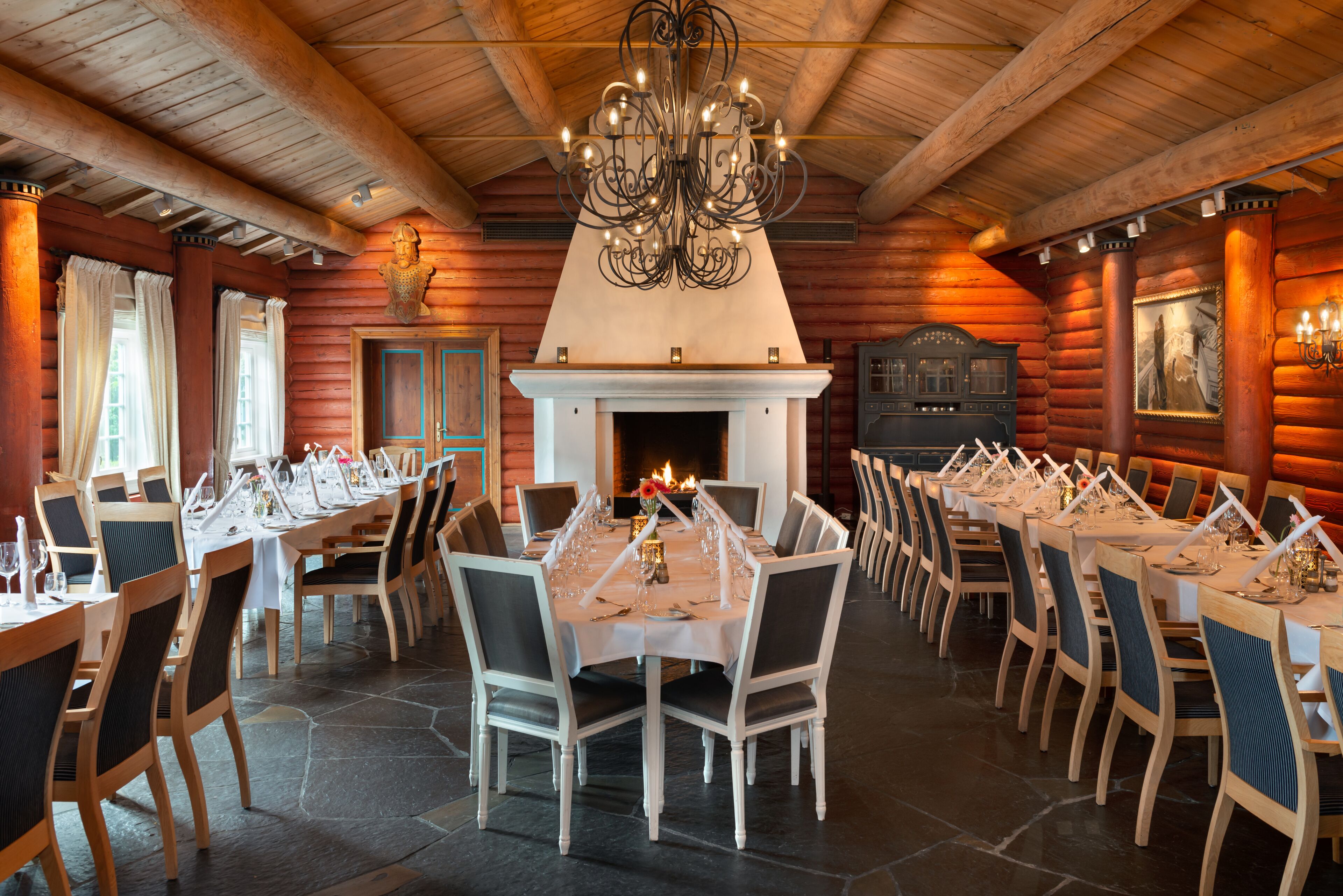 A log cabin-style restaurant with a fireplace, wooden tables, and chairs arranged for dining.