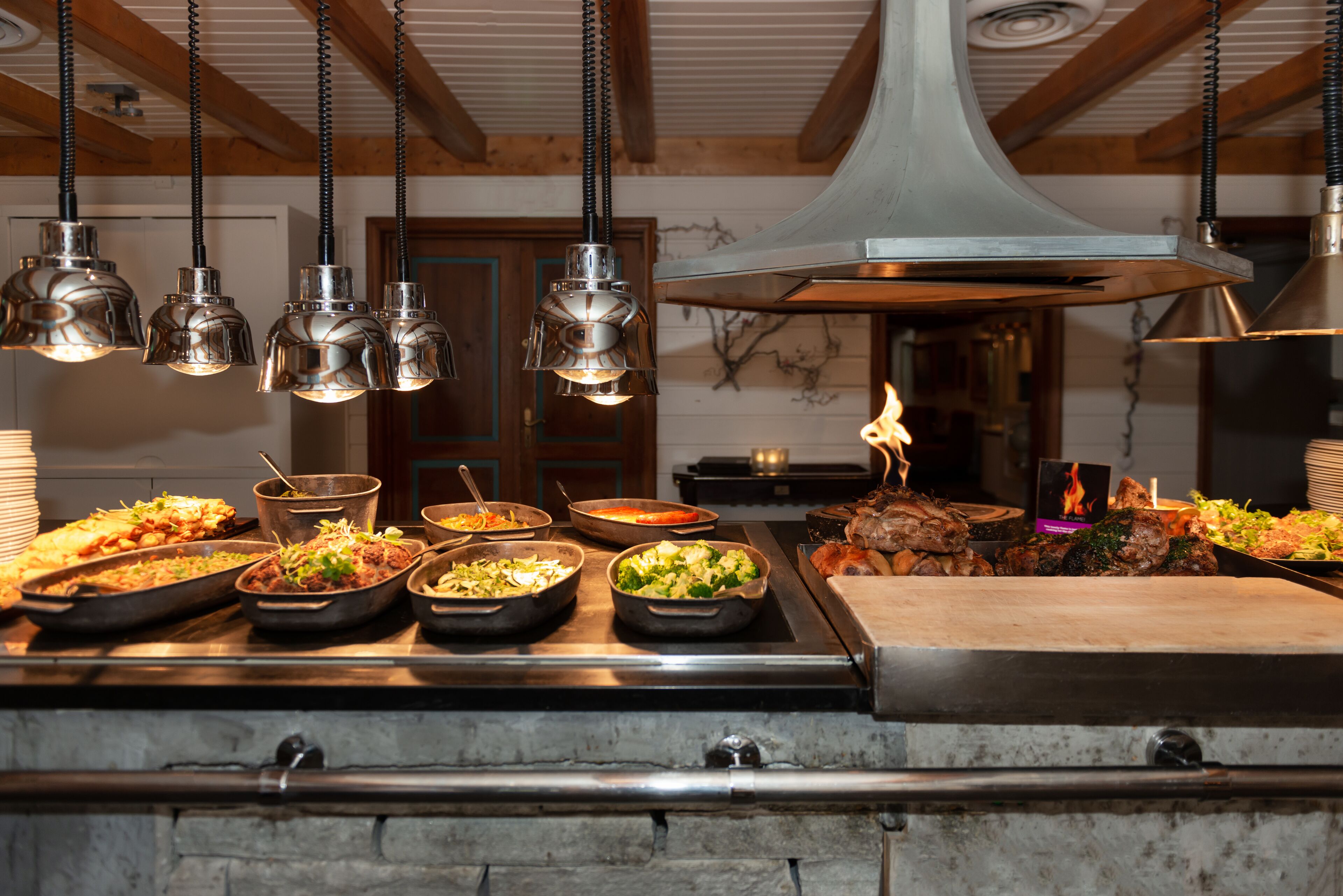 A buffet setup with various dishes and a large overhead industrial-style light fixture.