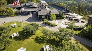 A lodge with a flag, a deck with outdoor seating, and a view of a lake and forest. - Quality Hotel Leangkollen (Asker)