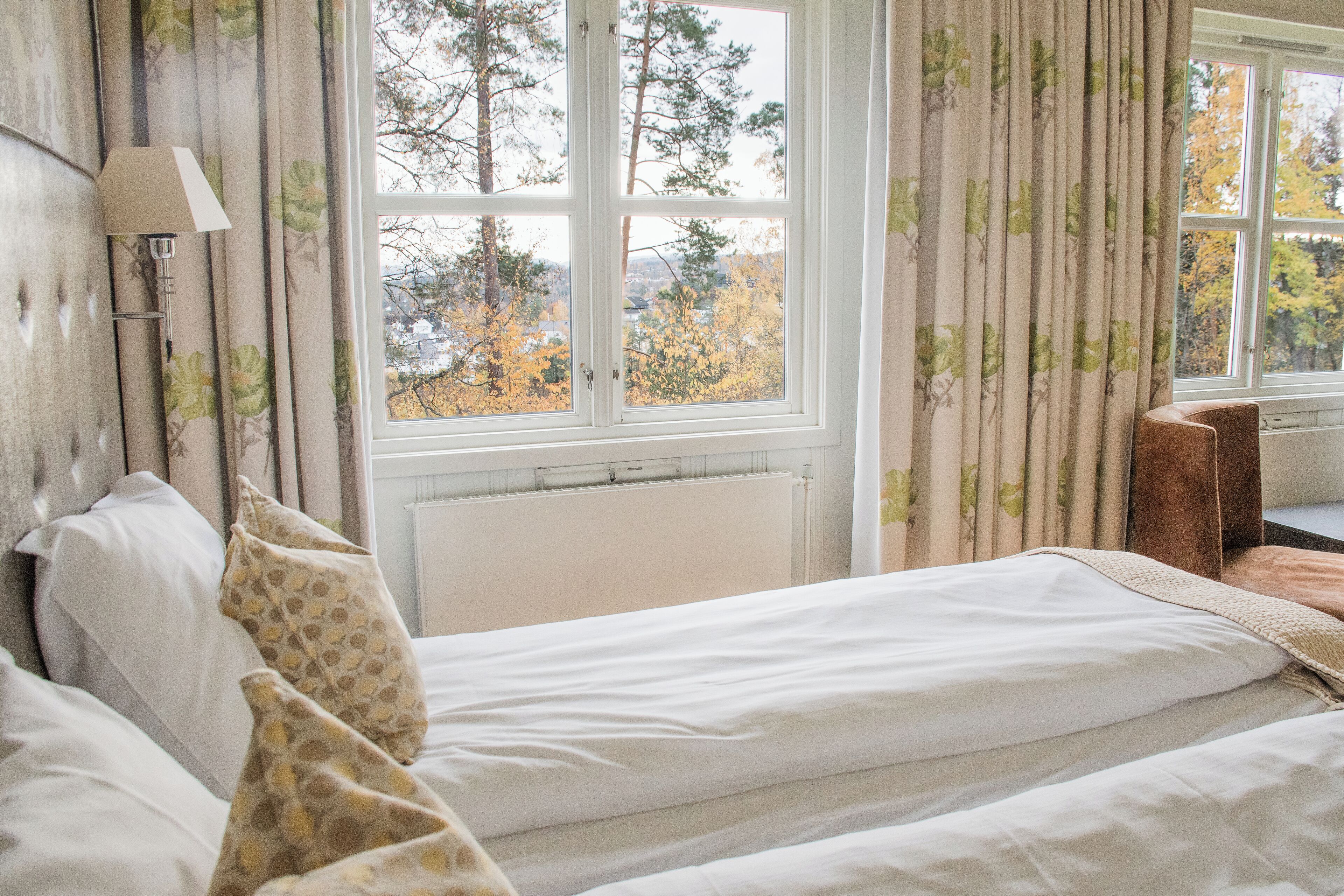 A bedroom with a bed, a nightstand, a lamp, and a window with curtains.