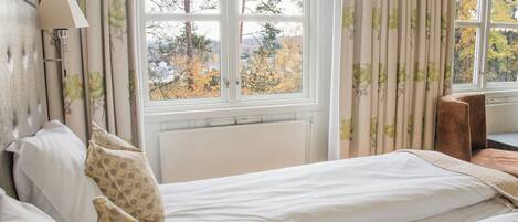 A bedroom with a bed, a nightstand, a lamp, and a window with curtains.