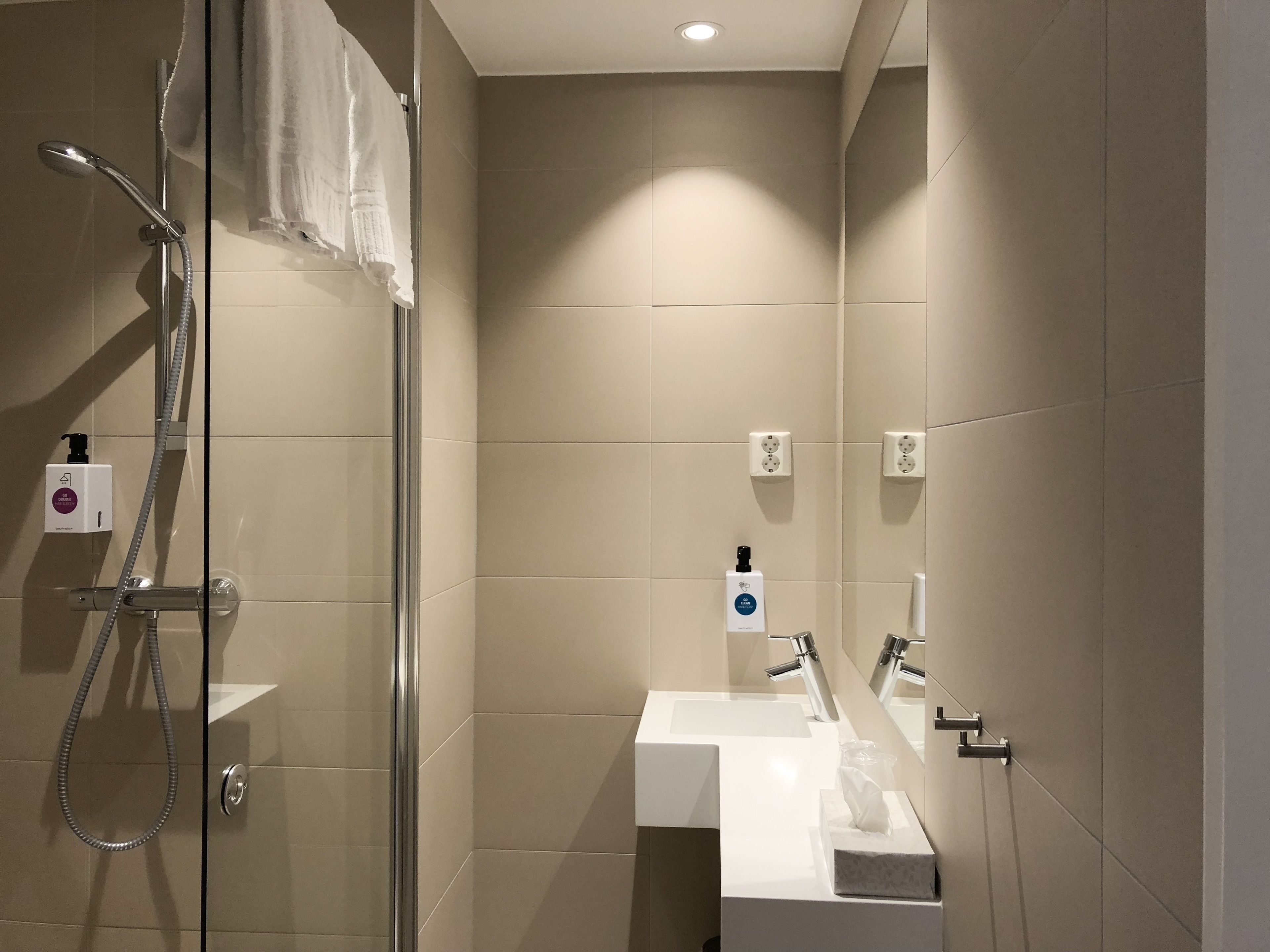 A modern bathroom with a glass shower enclosure, a white sink, and a mirror.
