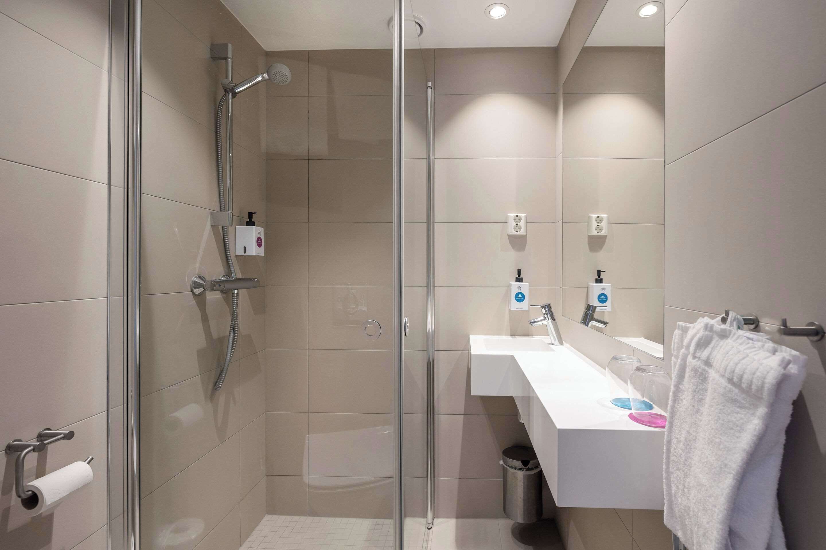 Un baño moderno con ducha envuelta en vidrio, un lavabo blanco con espejo y un perchero para toallas.
