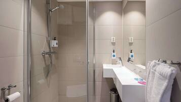 Un baño moderno con ducha envuelta en vidrio, un lavabo blanco con espejo y un perchero para toallas.