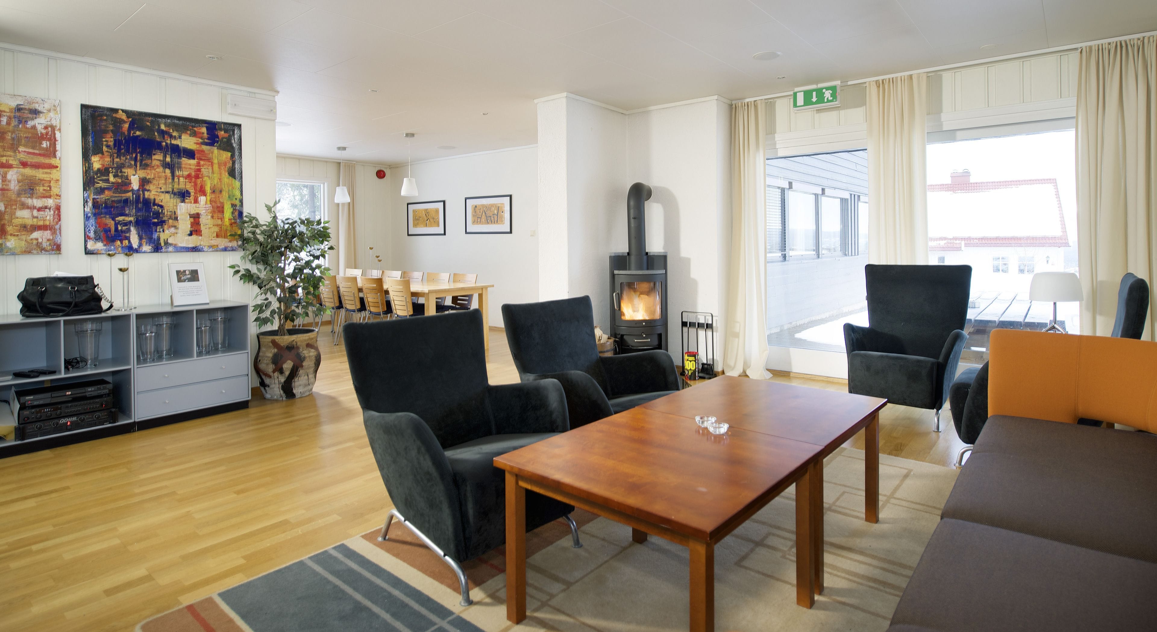 Una sala moderna con una mesa de madera, sillones negros, un sofá, una chimenea y un comedor con sillas y una mesa.