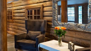 A log cabin interior with a dark upholstered armchair, a white table with a vase of flowers, and a large ornate mirror. - Quality Hotel Leangkollen (Asker)