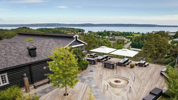 A wooden deck with outdoor seating, a fire pit, and a view of a lake. - Quality Hotel Leangkollen (Asker)