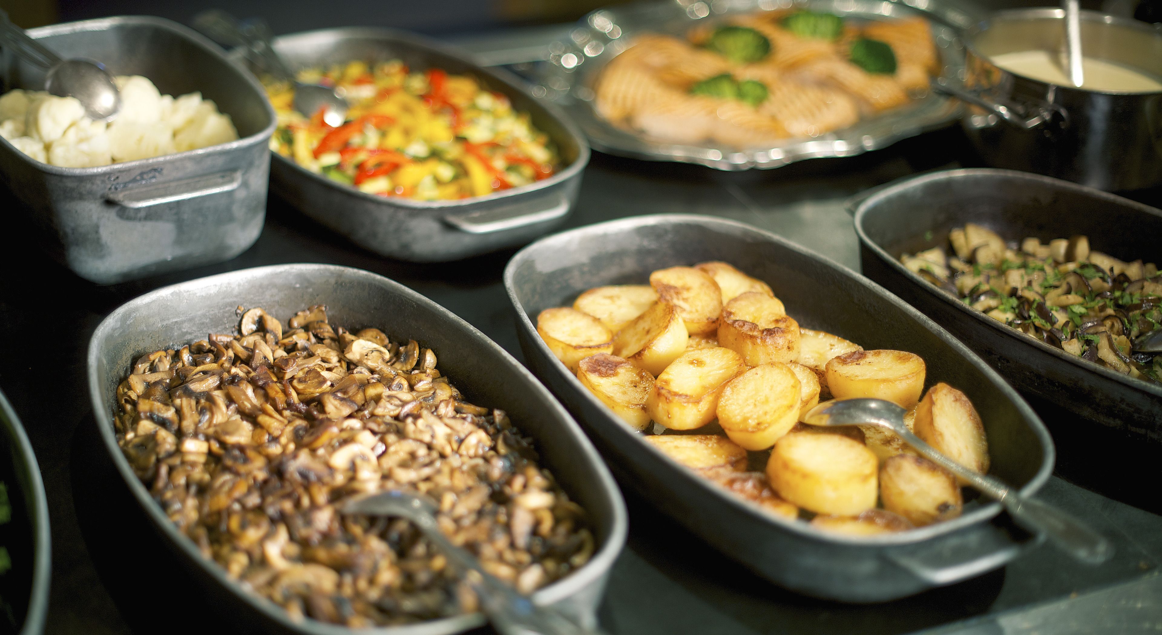 Un bufé con varios platos, incluyendo patatas, champiñones y un salteado de verduras.