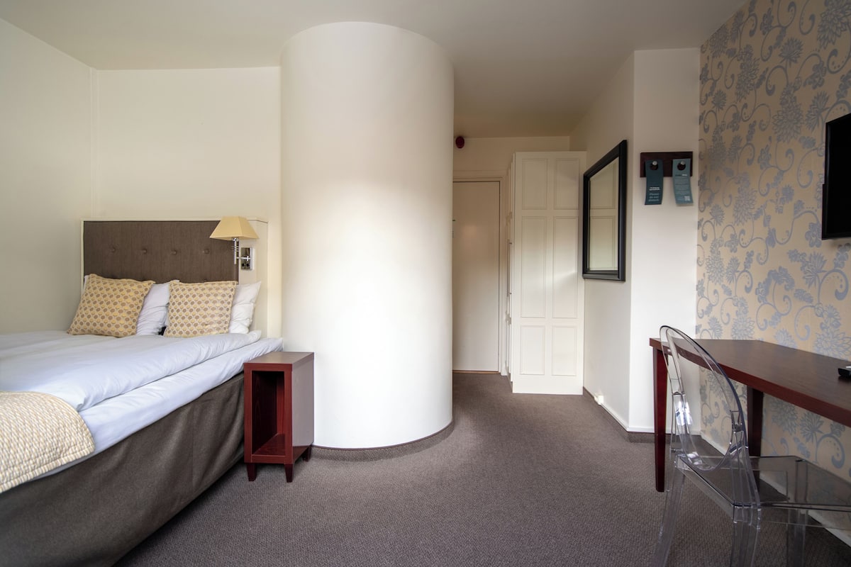 A hotel room with a bed, a nightstand, a desk, and a chair.