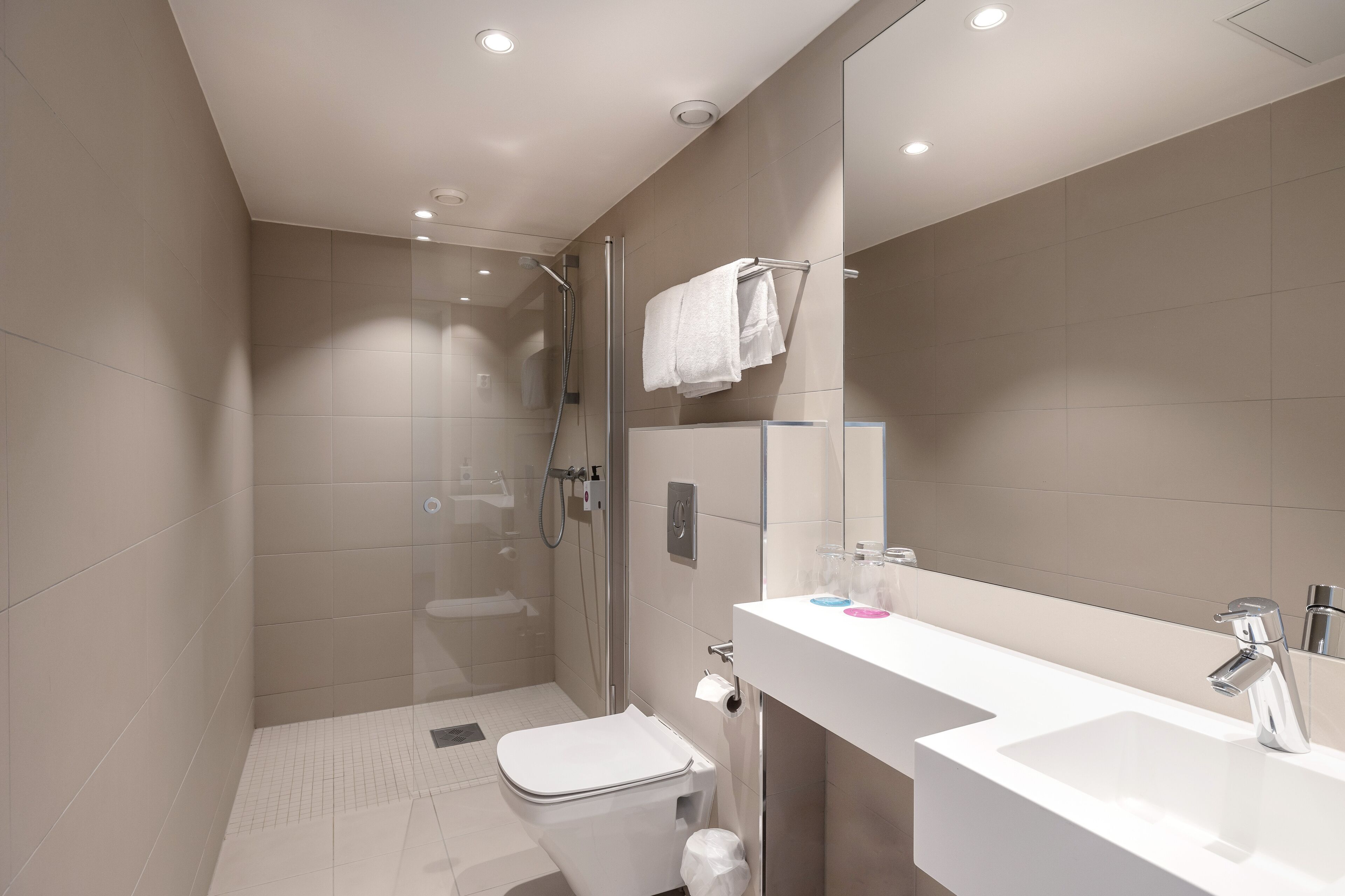 A modern bathroom with a glass-enclosed shower, a white sink, and a large mirror.