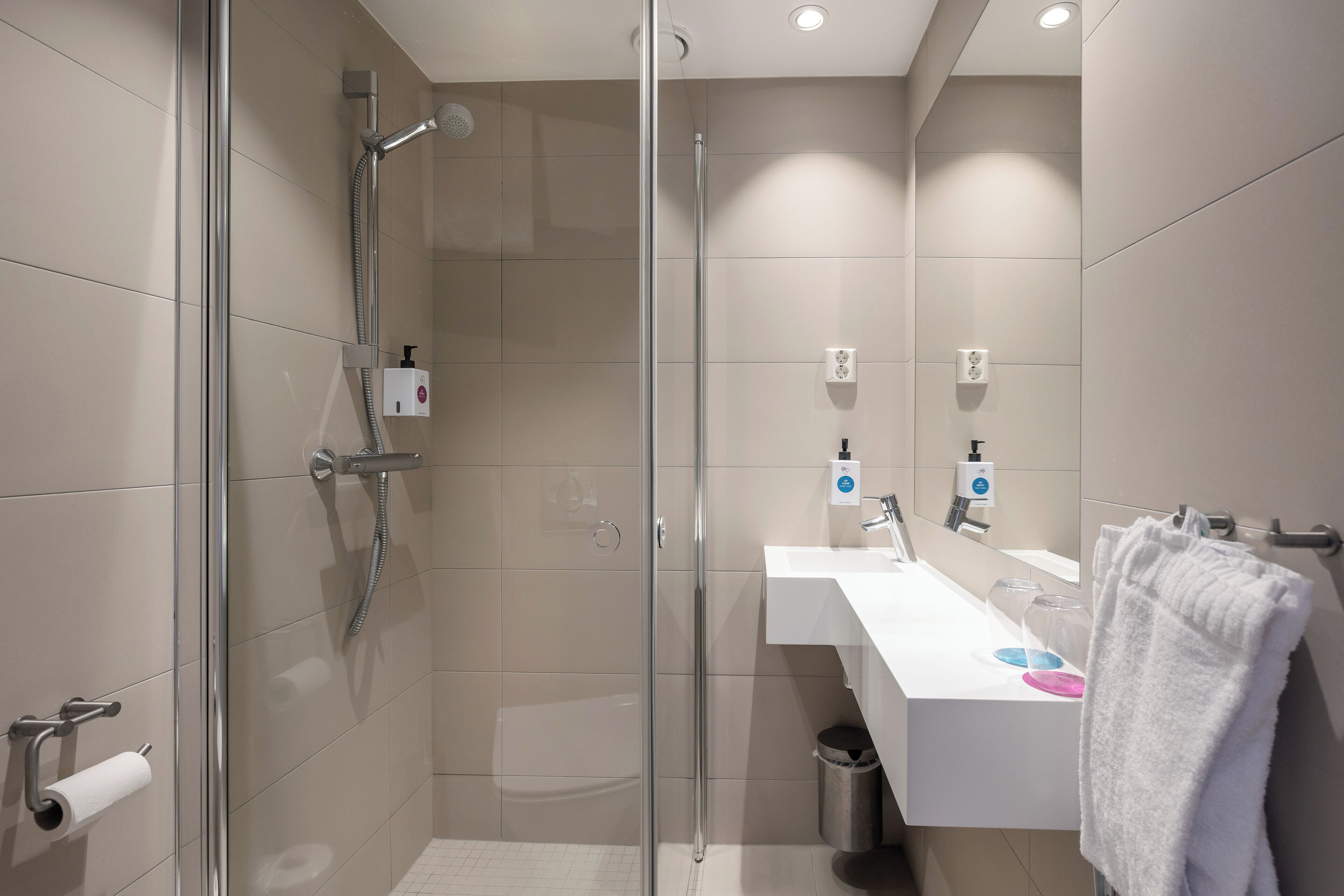 Un baño moderno con ducha envuelta en vidrio, un lavamanos blanco y un perchero para toallas.