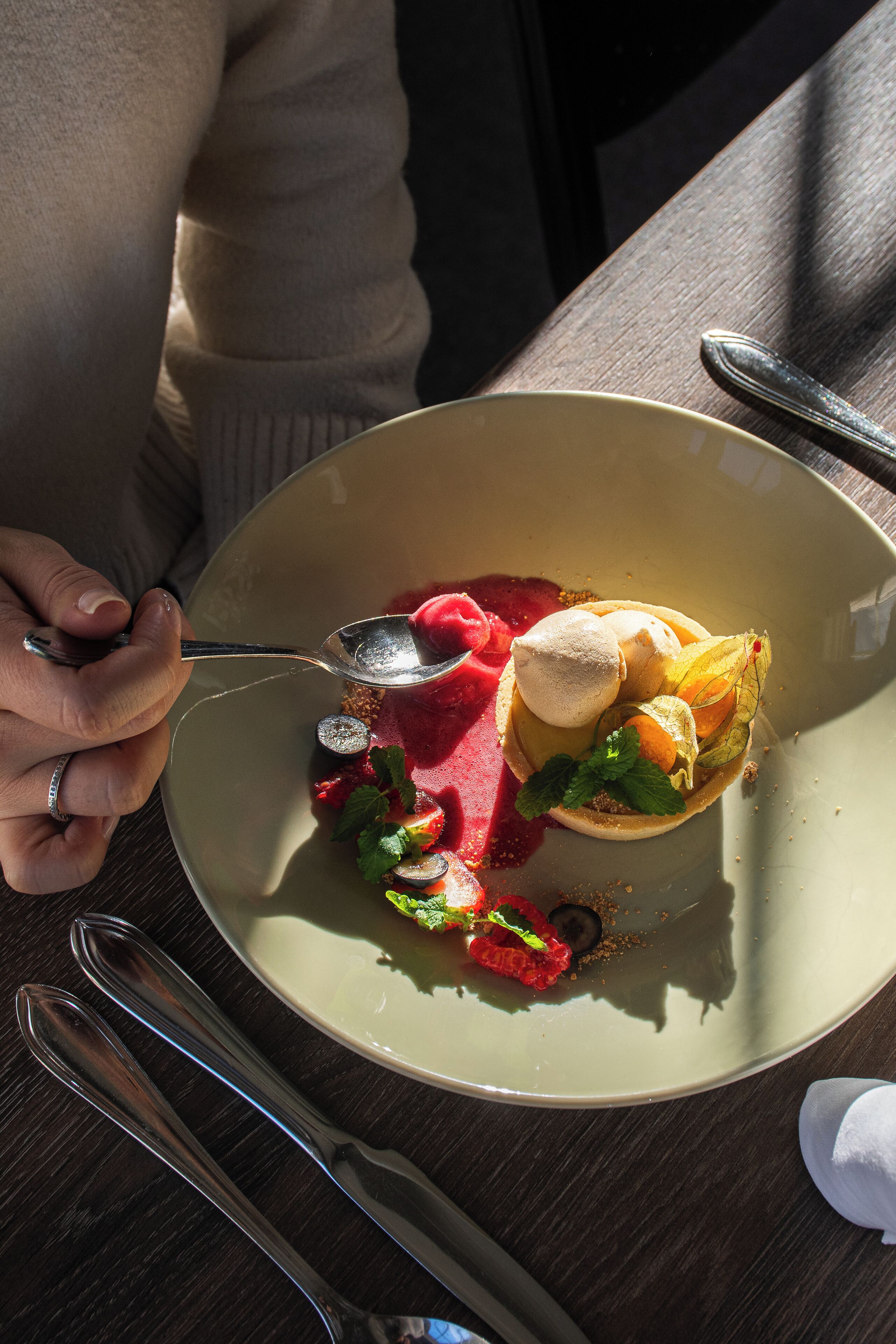 A dining table with a plate of food, a spoon, and cutlery.