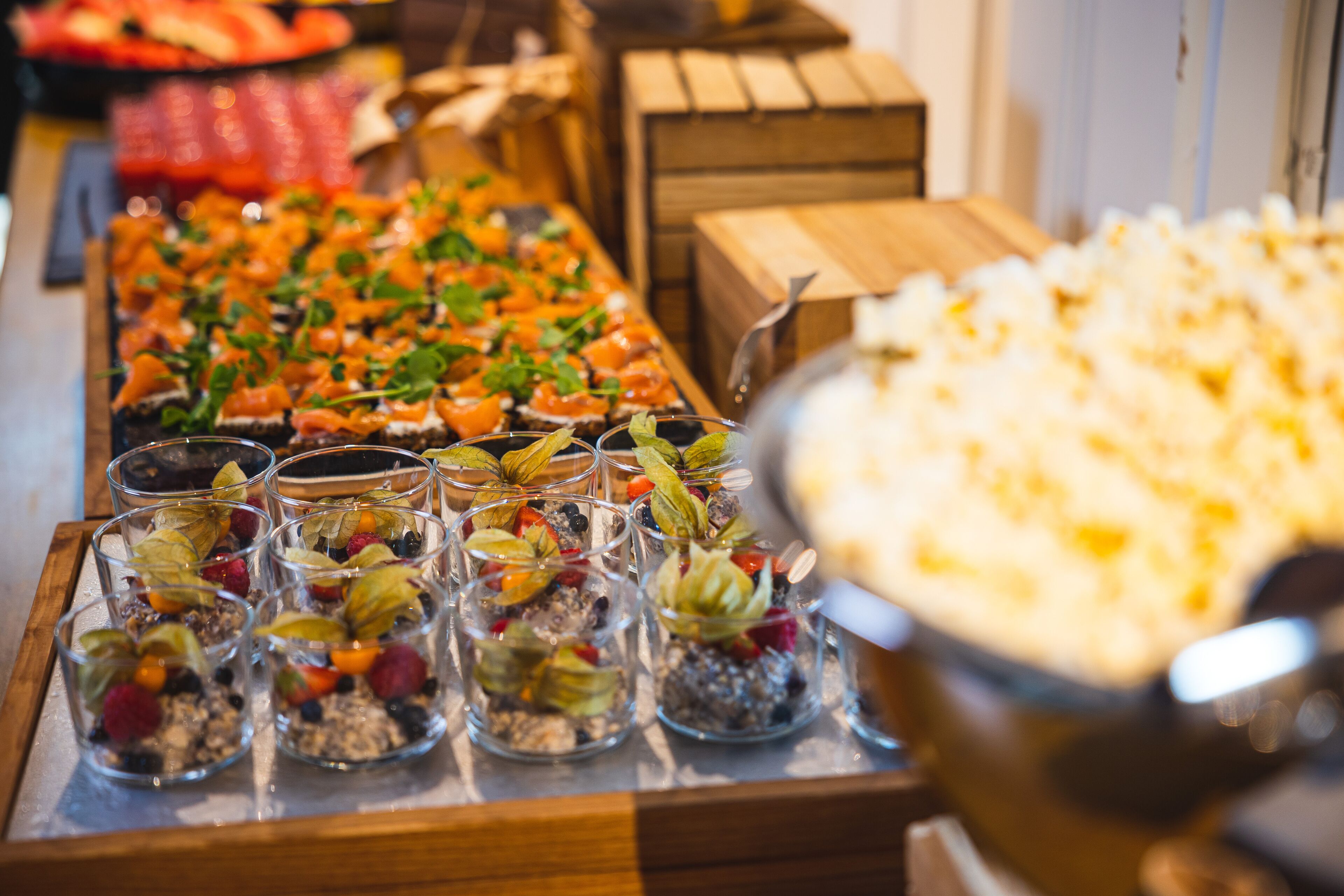 Una mesa de buffet con diversos alimentos, incluyendo un gran bol de palomitas de maíz y varios vasos con una mezcla de frutas y frutos secos.