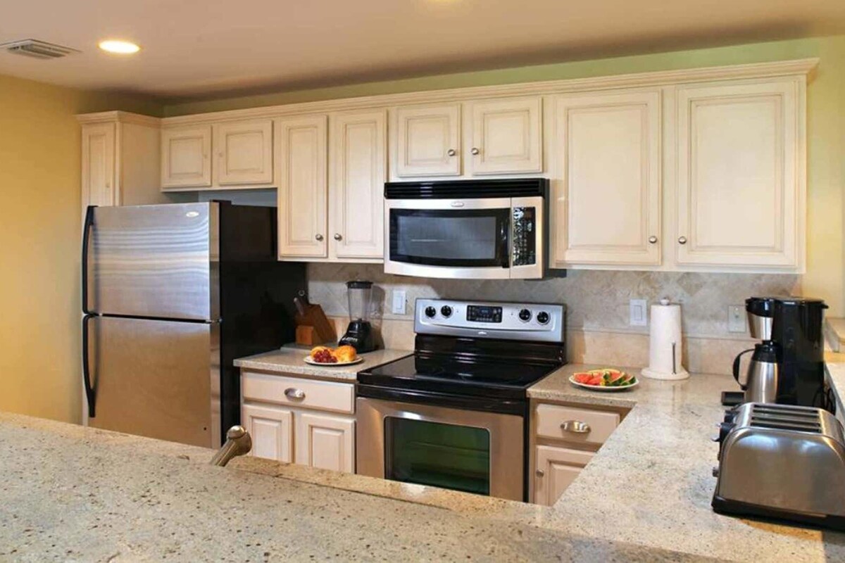 A kitchen with white cabinets, a stainless steel refrigerator, a microwave, an oven, a coffee maker, and a toaster.