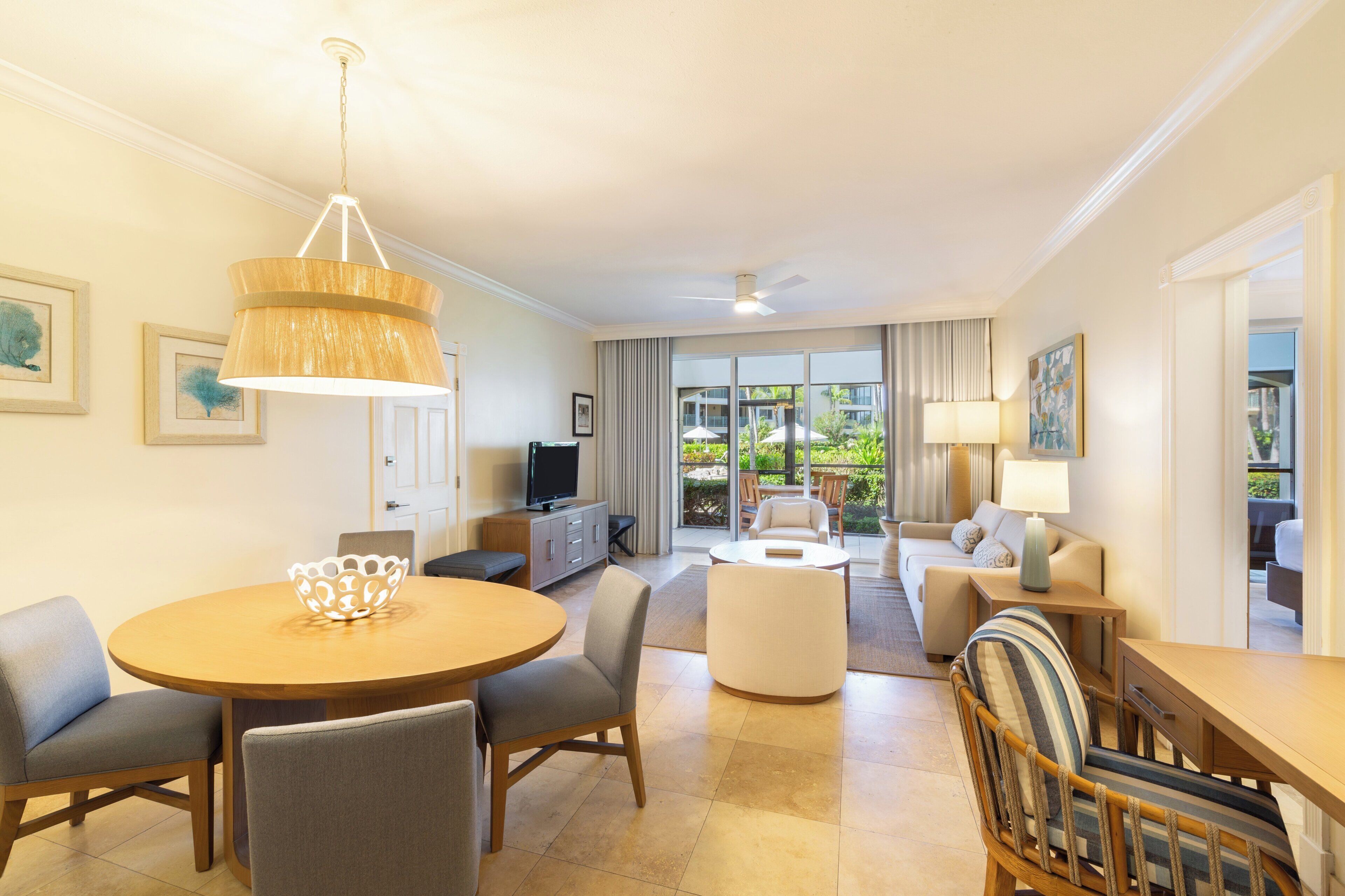 Habitación de hotel con zona de comedor, un sofá, televisor y vistas al exterior.