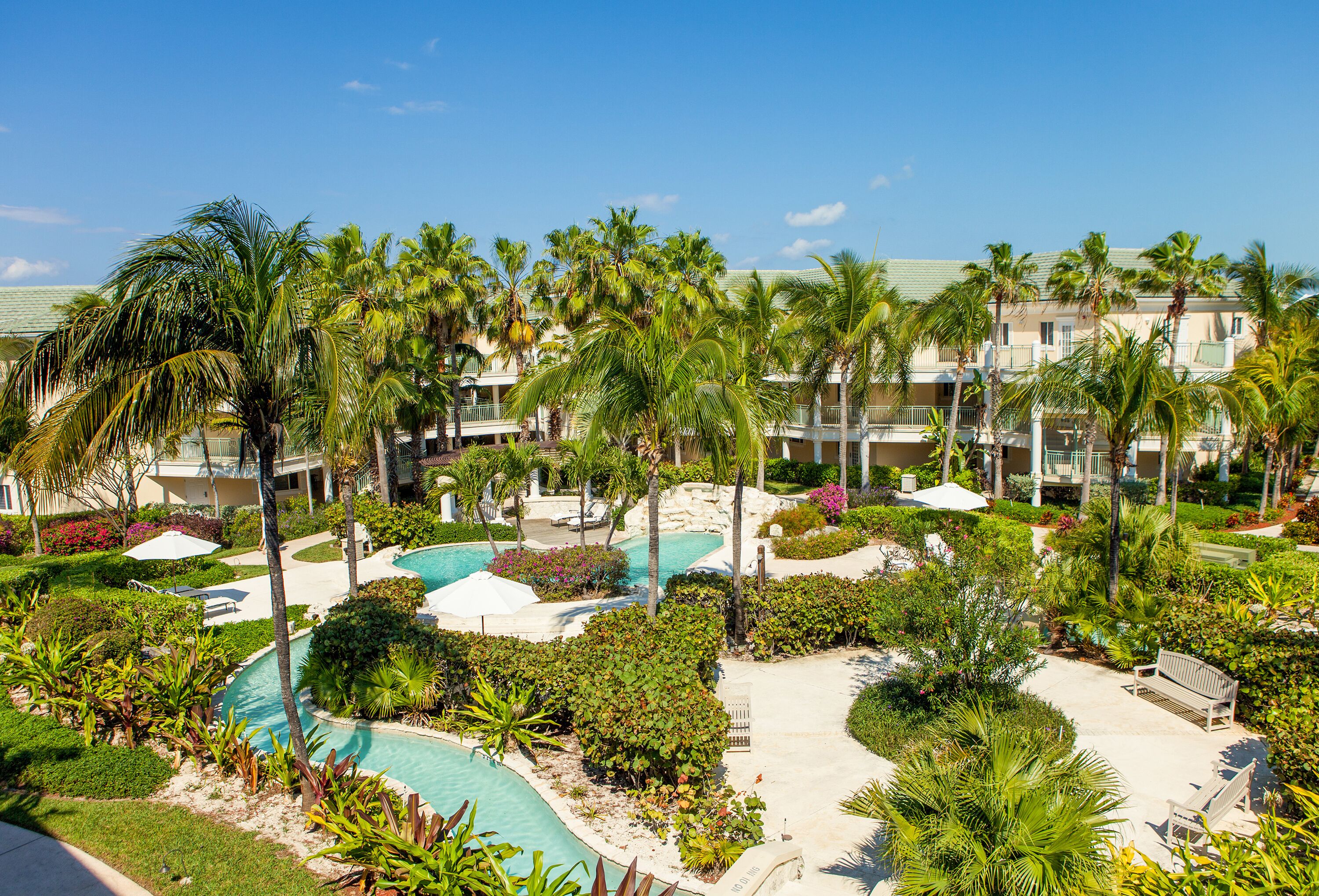 Un resort con varias piscinas, palmeras y un jardín bien cuidado.