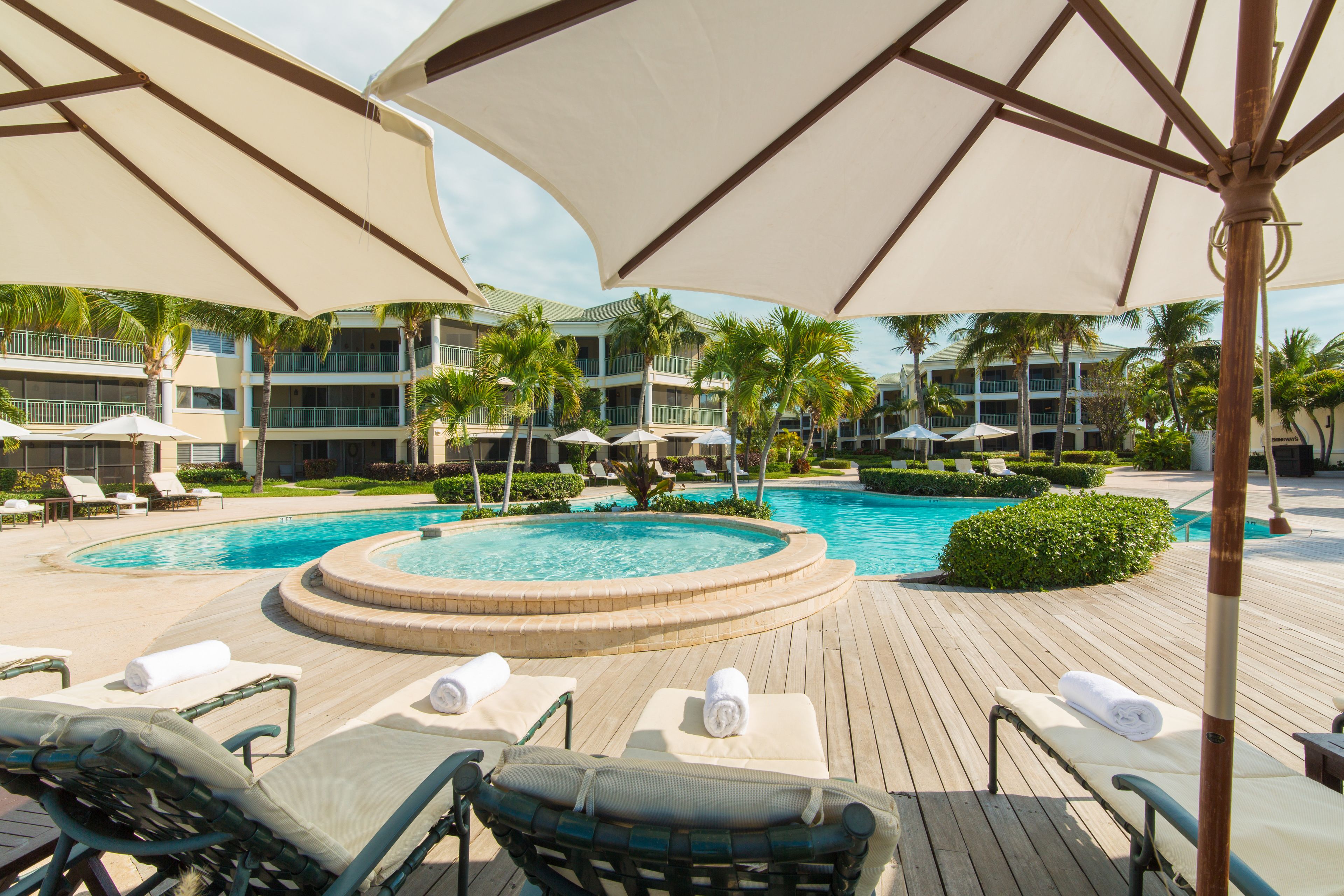 A poolside area with lounge chairs, umbrellas, and a hot tub.