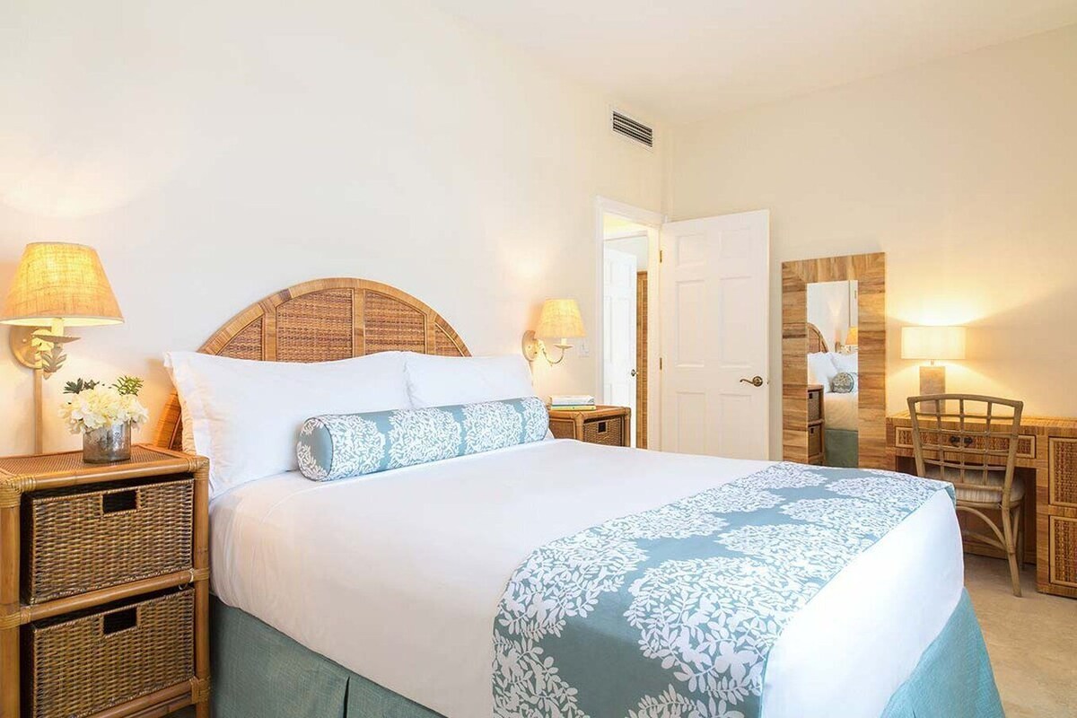 A neatly made bed with a headboard, two bedside tables with lamps, a mirror, and a chair.