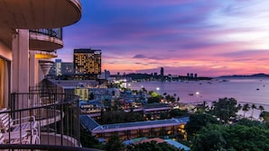 Un paisaje urbano costero al atardecer con un edificio destacado de ventanas iluminadas, un muelle y un balcón con vistas a la escena.