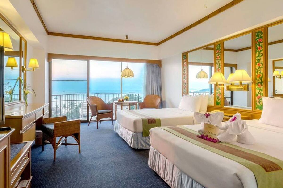 Une chambre d’hôtel avec deux lits, un bureau, une chaise, une petite table avec un vase et une vue sur l’océan.