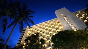 Un hotel de varios pisos con fachada uniforme, numerosos balcones y una estructura vertical central.