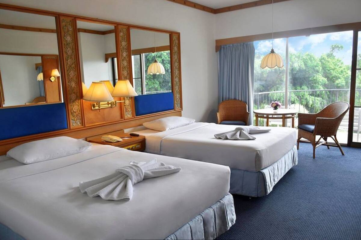 Une chambre d’hôtel avec deux lits, un coin salon comprenant une chaise et une table, et une grande fenêtre donnant sur un paysage verdoyant.