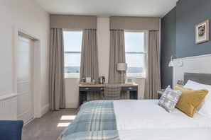 Habitación de hotel con cama, escritorio con lámpara, vista a la ciudad y ventana con cortinas.