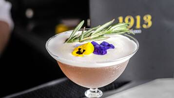 Een cocktail in een martini-glas, versierd met rozemarijn en een bloem, op een marmeren oppervlak.